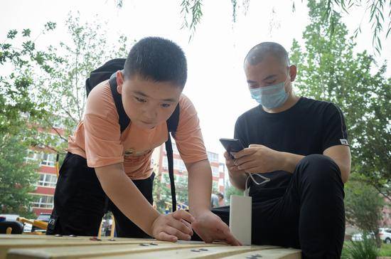 　　2019年7月20日，北京大学人民医院清河分院附近的小区里，路子宽在逗长椅上的蚂蚁，父亲在一旁打电话联系病友。 新京报记者 陈婉婷 摄